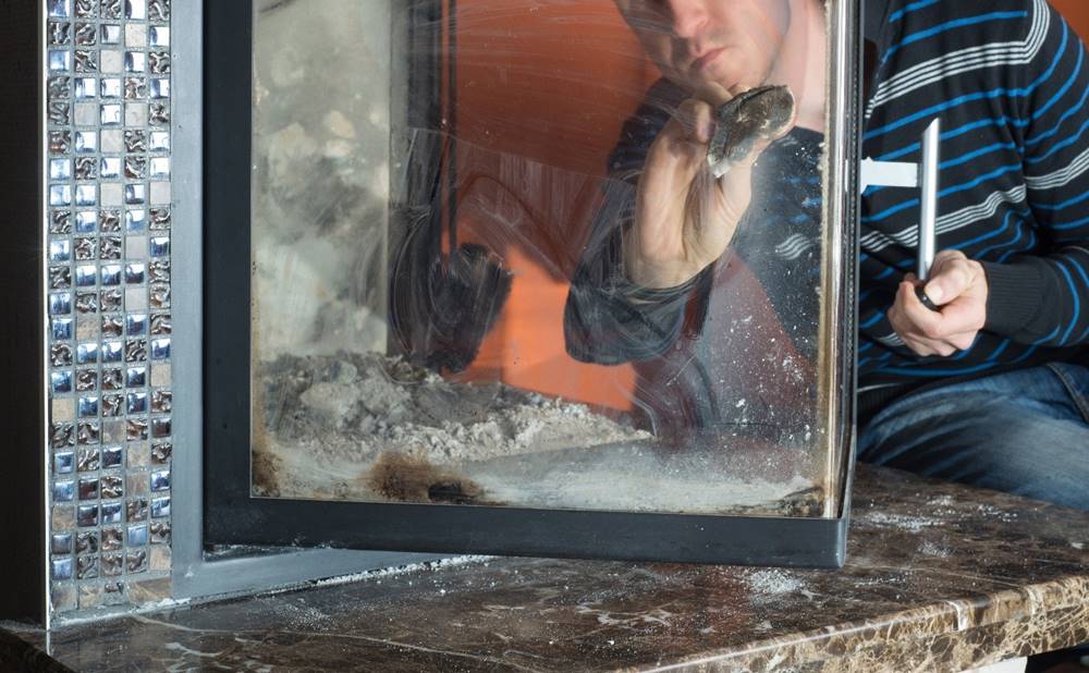 Mann reinigt Glasfront eines Kaminofens
